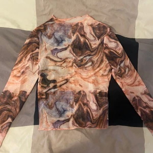 Mönstrad långärmad topp - Säljer en cool långärmad topp med ett unikt mönster i olika nyanser av brunt, beige och lila. Toppen är tight och har en hög hals. Perfekt för höst och vinter och vardags. Materialet känns som syntet och är stretchigt och bekvämt. oanvänd