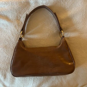 Brun handväska  - En lite större handväska med guldiga detaljer för dig som gillar att ha mycket saker med dig utan att väskan inte går ihop.