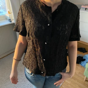 Svart t-shirtskjorta med blommor i spets - Svart t-shirtskjorta med blommor i spets. Köpt secondhand i tyskland, märke och storlek saknas men sitter som en small.