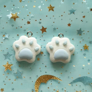 2st vit och blå djur tassar berlock  - Berlocker, hängsmycke, Motiv: tassar  Färg: vit med blå detalj  Antal: 2st Skick: oanvända,  Går att använda till smyckestillverkning, tex sätta på halsband, armband eller göra örhängen av dem. 