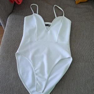 White Bodysuit - En elegant vit baddräkt från Boohoo med smala axelband och en djup v-ringning. Baddräkten har en enkel och stilren design, perfekt för sommar. festival, bröllop... bär bara 4 timmar. ä 100% ny. 