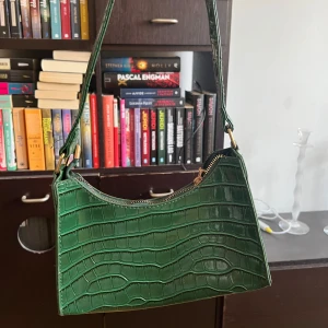 grön väska - Grön axelväska, ormskinns mönstrad. Plastig yta. Guldiga detaljer. Ca 20cm.