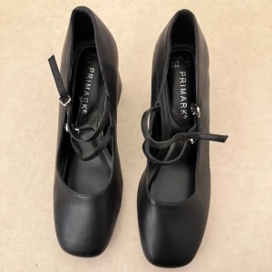 Svarta klackskor med remmar från Primark - Säljer ett par svarta klackskor från Primark med fyrkantig tå och justerbara remmar över foten. Skorna har en stabil klack och är tillverkade i syntetmaterial. Perfekta för dig som vill ha en klassisk och stilren look. I storlek 38