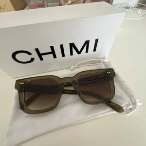 Olivgröna solglasögon från CHIMI 04 - Snygga solglasögon från CHIMI i en olivgrön, transparent plast med fyrkantig form och bruna tonade glas. Klassisk och trendig modell 04 med CHIMI-logga på skalmen. Perfekt accessoar för soliga dagar.