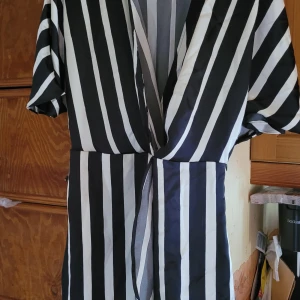 Svartvit randig omlottklänning - Säljer en svartvit Tunika med vertikala ränder och korta ärmar. Klänningen har en djup v-ringning . Perfekt för dig som gillar en stilren och trendig look.