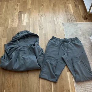 Grå mjukisbyxor från Nike och tröja  - Säljer ett par grå mjukisbyxor från Nike med dragsko i midjan och praktiska fickor på sidorna. Byxorna har en avslappnad passform och är perfekta för chill eller träning. Matchande hoodie finns också om du vill ha ett set.