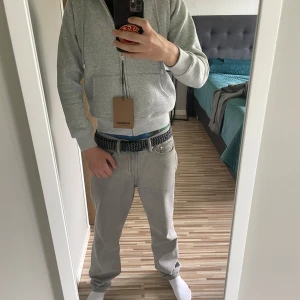 Grå zip-hoodie från Burberry - Säljer en grå hoodie med dragkedja från Burberry. Klassisk modell med känguruficka och justerbar huva med Burberrys ikoniska rutiga mönster på insidan. Stora ribbade muddar och snygg metall-dragkedja med Burberry-logga.