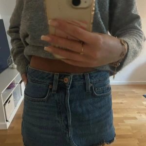 Jeanskjol med rå kant - Säljer en klassisk blå jeanskjol med rå, fransig kant nertill. Kjolen har fem fickor, bälteshällor och stängs med knapp och dragkedja framtill. Perfekt för dig som gillar en avslappnad och trendig stil.