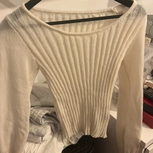 Vit ribbad stickad tröja - Säljer en vit stickad tröja med ribbat mönster och lång ärm. Tröjan har en något vid halsringning och är perfekt för lager-på-lager. Enkel och stilren design som passar till det mesta. Aldrig använd
