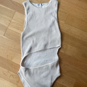 Vit ribbad baddräkt från Zara - Säljer en vit ribbad body  från Zara i storlek XS. bodyn har en asymmetrisk skärning med öppen midja och rund halsringning. 