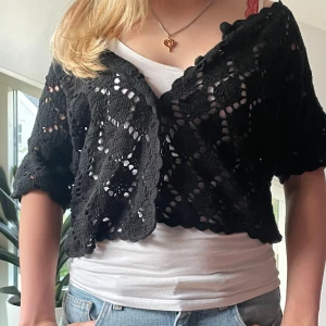 Svart virkad kofta - Säljer en svart, virkad kofta med kort ärm och croppad passform. Koftan har ett öppet mönster och är perfekt att slänga över ett linne eller t-shirt. Superfin detalj till din outfit! BOLERO