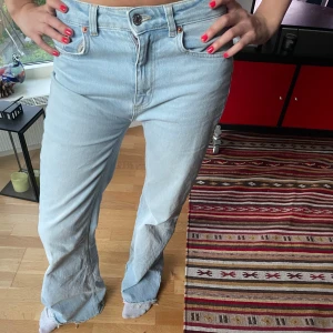 Ljusblå bootcut jeans - Säljer ett par ljusblå jeans med bootcut passform och råa kanter nertill. Klassisk femficksmodell med knapp och dragkedja framtill. Perfekta för en avslappnad och trendig look. UNGEFÄR 28/32 står inte 