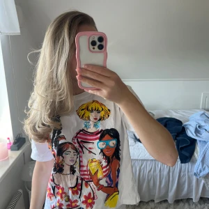 Vit t-shirt med färgglatt tryck - Säljer en vit t-shirt med ett färgglatt tryck av fyra stiliserade kvinnor i olika kläder och accessoarer. T-shirten har korta ärmar och en rund halsringning. Perfekt för en färgglad och unik stil!🩷🥺🫶🏼