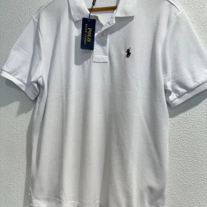 Vit ziptröja från Polo Ralph Lauren - Klassisk vit ziptröja från Polo Ralph Lauren med dragkedja framtill och två fickor. Tröjan har lång ärm och en liten broderad logga på bröstet. Perfekt för en stilren och avslappnad look.
