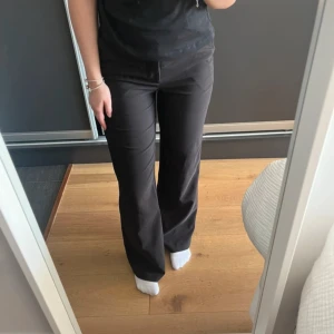 Svarta kostymbyxor med knappar - Säljer ett par svarta kostymbyxor med hög midja och raka, något utsvängda ben. Byxorna har dekorativa knappar i midjan och fickor framtill. Perfekta för en stilren och klassisk look. Aldrig använda, nypris 649!