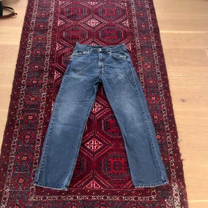 Blå jeans från Boss - Säljer ett par klassiska blå jeans från Boss med raka ben och normal passform. Jeansen har fem fickor, bälteshällor och metallknapp framtill. Boss-logga på bakfickan och metallbricka bak i midjan.