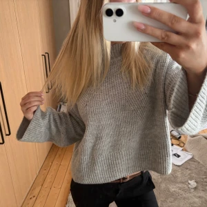 Grå stickad tröja från Gina Tricot - Säljer en ljusgrå stickad tröja från Gina Tricot med breda ärmar och avslappnad passform. Tröjan har ribbad struktur och hög hals, perfekt för lager-på-lager-stil. Supermjuk och enkel att matcha till olika outfits.