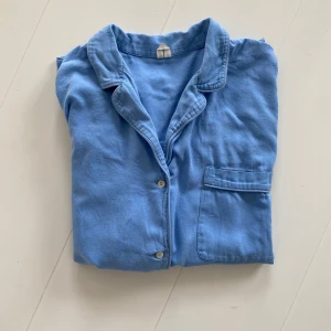 Pyjamas blå arket bomull - Säljer en klassisk blå pyjams set med lång ärm och knäppning framtill. Skjortan har en bröstficka och mjukt, tunt tyg som känns skönt mot huden. Perfekt för en avslappnad och stilren look.