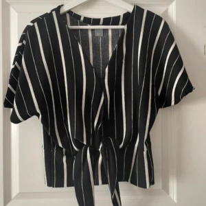 Svartvit randig topp med knyt - Snygg svart topp med vita ränder. Knytning framtill och korta ärmar ger en avslappnad men trendig look. Perfekt till jeans eller kjol för en cool stil. Aldrig använd.
