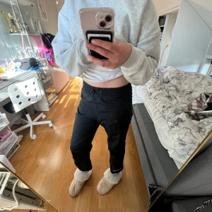 Svarta täckbyxor från McKinley - Svarta täckbyxor från McKinley med resår i midjan och dragsko. Byxorna har raka ben och är perfekta för kalla dagar. Logotypen syns nere vid benslutet. Snygga och funktionella för hösten. (Står ett efternamn på lappen)