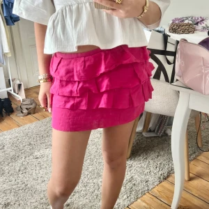 Rosa volangkjol från COS - Säljer en superfin rosa kortkjol med flera lager volanger. Kjolen har en härlig färg och är perfekt för dig som vill sticka ut lite extra. Passar perfekt till sommaren och är lätt att matcha med olika toppar.