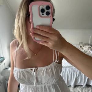 Vit linnetopp med tunna axelband  - Säljer en söt vit linnetopp från H&M med tunna axelband och knytning framtill. Toppen har en luftig och lätt passform, perfekt för varma dagar. Enkel och stilren design som passar till mycket.