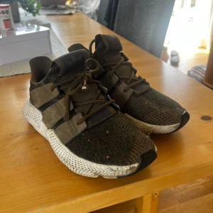 Adidas sneakers i olivgrönt - Säljer ett par Adidas sneakers i olivgrönt med svarta detaljer och vit, mönstrad sula. Skorna har snörning och en sportig design med stickad ovandel.  Skorna är knappt använda och bara lite smutsiga under, annars i princip nyskick!