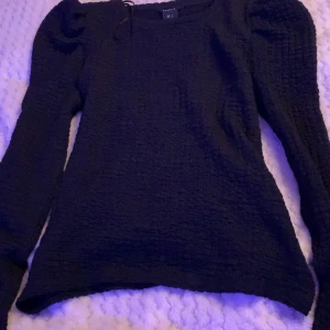 Svart strukturerad topp från Lindex - Säljer en svart långärmad topp från Lindex i storlek S. Toppen har puffiga axlar och är gjord i ett strukturerat, stretchigt material som ger en snygg passform. Perfekt för dig som gillar stilrena och trendiga plagg.