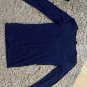 Mörkblå långärmad topp med spetsdetalj - Säljer en mörkblå långärmad topp  med vacker spetsdetalj framtill. Tunn och mjuk i materialet, men jag har sytt in den i midjan på både sidorna. Som man ser i foto två. Det går att sortera upp om man inte gillar det 