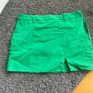 Grön kortkjol från Stradivarius - Snygg grön kortkjol från Stradivarius med bälteshällor och liten slits framtill. Kjolen har en dold dragkedja i sidan och är perfekt för dig som gillar färg. Enkel och stilren design som passar till många olika looks.