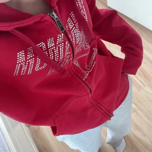 Hoodie med dragkedja  - Säljer en röd hoodie från Russell med dragkedja och glittrande strasstext framtill. De går inte å få tag i längre. Orginal priset e ungefär 500kr. Är i storlek xs.