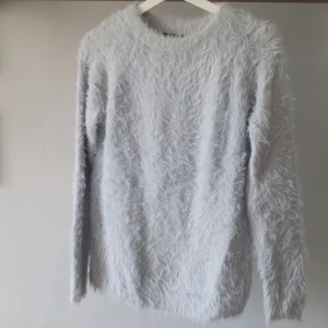 Ljusblå fluffig tröja från Gina Tricot - Supermjuk och fluffig ljusblå tröja från Gina Tricot. Tröjan har lång ärm och rund halsringning, perfekt för att hålla sig varm och snygg under kyliga dagar. Materialet är lurvigt och ger en mysig känsla.