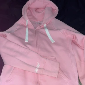 Rosa hoodie med dragkedja - Säljer en ljusrosa hoodie från Russemerch i storlek M. Tröjan har dragkedja framtill, huva med vita snören och två fickor. Perfekt för en avslappnad stil och enkel att matcha med jeans eller leggings. Den är endast använd ett fåtal gånger, så den är principt helt oanvänd! 