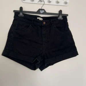 Svarta jeansshorts från H&M - Svarta jeansshorts från H&M med klassisk femficksdesign och uppvikta benslut. Modellen har normal passform och stängs med knapp och dragkedja. Perfekta för sommardagar och enkla att matcha med olika toppar.