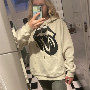 Beige hoodie med Rolling Stones-tryck från H&M - Säljer en beige hoodie från H&M med det klassiska Rolling Stones-trycket i svart på bröstet. Tröjan har huva och en magficka. Perfekt för en avslappnad stil. Det står M men den är liten för sin storlek.