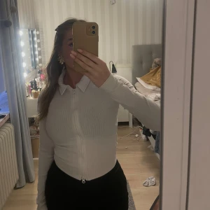 Vit ribbad ziptröja  - Säljer en vit ribbad ziptröja. Tröjan är croppad med lång ärm, krage och dragkedja framtill. Det finns två dragkedjor - så man kan välja själv hur tröjan ska vara öppen eller stängd. Perfekt till jeans eller kjol för en clean look.