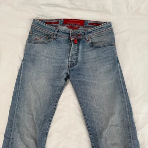 Jacob Cohen Jeans - Säljer ett par ljusblå jeans från Jacob Cohen med röda sömmar och detaljer. Perfekta för dig som gillar snygga och unika jeans. Dem är i toppskick! Säljer för dem är tyvärr för små!