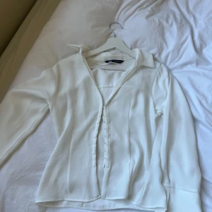 Vit långärmad blus från Zara - Blusen har knappar framtill och en lätt figursydd passform. Inte genomskinlig 