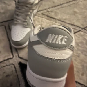 Nike Dunk Low i grått och vitt - Säljer ett par Nike Dunk Low i stilren grå och vit färg. Skorna har klassisk design med perforerad tå, snörning och låg profil. Perfekta för dig som gillar sneakers med enkel och clean look.