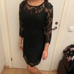 Svart spetsklänning från Guess - Säljer en svart klänning från Guess med vacker spets och trekvartsärm. Klänningen har rund halsringning och är fodrad med ett slätt innerfoder. Perfekt för dig som gillar eleganta detaljer och klassisk stil. Klänningen har en lång klänning där bak som ger fina former