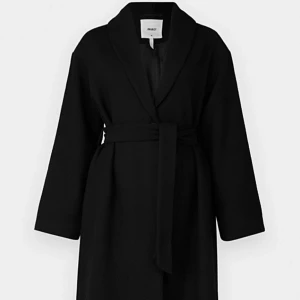 Svart kappa med bälte från Object - Säljer en stilren svart kappa från Object med bälte i midjan. Jackan har lång ärm och klassisk krage, perfekt för dig som gillar en enkel och tidlös look. Passar till många olika outfits.
