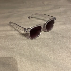 Transparenta solglasögon med svarta glas - Snygga solglasögon med transparent båge och mörka, nästan svarta glas. Rektangulär form som ger en modern vibe och passar till många olika stilar. Perfekta för soliga dagar och en cool look.