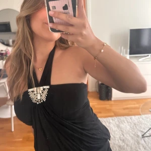 Svart halterneck topp med dekorativa pärlor - Säljer en svart halterneck topp med snygg drapering och dekorativa pärlor framtill. Toppen har en elegant form och knyts i nacken. Storlek S