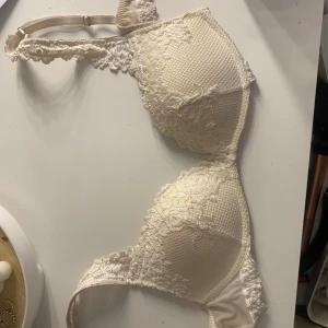 beige push up bh intimissimi - Säljer en vit bh intimissimi med vacker spetsdetalj och vadderade kupor. Bh:n har justerbara axelband och en klassisk knäppning bak. Perfekt för dig som gillar romantiska detaljer och en feminin look.