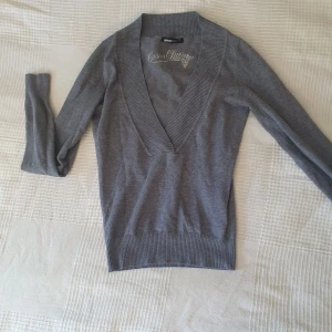 Grå v-ringad stickad tröja från Gina Tricot - Säljer en grå stickad tröja från Gina Tricot med djup v-ringning och ribbade kanter. Perfekt för lager-på-lager och enkel att matcha med olika outfits. Mjuk och skön kvalitet.💘