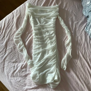 Vit offshoulder-klänning från Gina Tricot - Supersnygg vit kortklänning från Gina Tricot med draperad effekt och offshoulder-ärmar. Klänningen har en figurnära passform men strechig och är tillverkad i ett mjukt, syntetiskt material. Perfekt för dig som vill sticka ut med en elegant look. Passar bra som studentklänning. Användes endast en gång. 