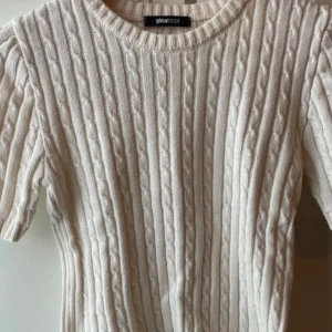 Vit kabelstickad tröja från Gina Tricot - Säljer en vit kabelstickad tröja från Gina Tricot med korta ärmar och rund halsringning. Tröjan har en klassisk, ribbad struktur och är perfekt för en stilren look.
