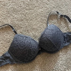 Grå spets-bh från H&M - Säljer en grå bh från H&M med vacker spets över hela kuporna. Bh:n har justerbara axelband och en klassisk knäppning bak. Perfekt för dig som vill ha något både snyggt och bekvämt.
