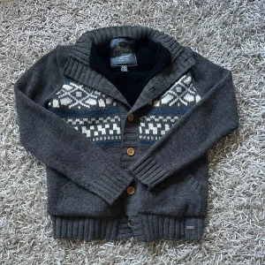 Stickad kofta från Diesel - Mysig mörkgrå stickad kofta från Diesel med klassiskt mönster i vitt och blått över bröstet. 