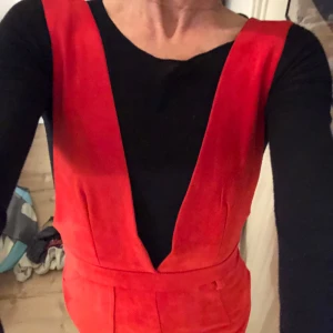 Röd klänning med djup v-ringning både fram och bak - Säljer en röd kortklänning med djup v-ringning både fram och bak. Den är figurnära och har en markerad midja. Perfekt för dig som vill sticka ut med en färgstark look.